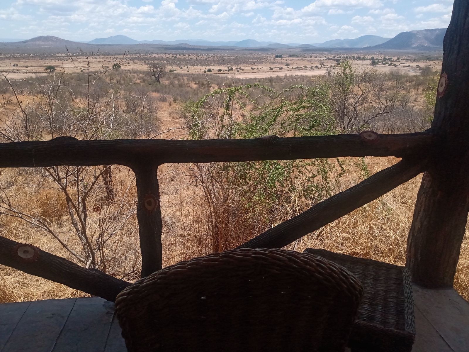 A wicker chair beside a lodge deck railing looking out over dry bush, Ruaha National Park